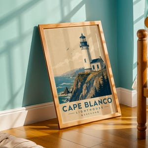 May include: A framed vertical art print featuring a stylized illustration of the Cape Blanco Lighthouse in Oregon. The image depicts a white lighthouse on a cliff overlooking the ocean with dark green trees, blue water, and the text CAPE BLANCO LIGHTHOUSE OREGON.