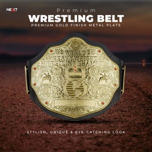 Könnte beinhalten: Ein goldfarbener Wrestling-Gürtel mit einem schwarzen Lederriemen. Der Gürtel weist aufwendige Details auf, darunter die Worte "WORLD HEAVYWEIGHT WRESTLING CHAMPION". Rote Akzente sind sichtbar. Der Text "WRESTLING BELT" steht oben.