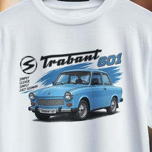 Könnte beinhalten: Ein weißes T-Shirt mit einer Grafik eines hellblauen Trabant 601 Autos. Das Design enthält den Text Trabant 601, ein kreisförmiges Logo und die Worte SIMPLY CLEVER. SIMPLY EAST GERMAN. Das Auto ist mit einem Frontgrill, Scheinwerfern und Stoßstange abgebildet.