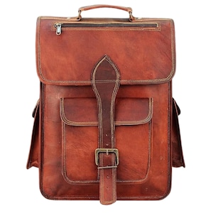 Può includere: Zaino in pelle marrone con maniglia superiore, tasca frontale e chiusura con fibbia regolabile. La borsa presenta uno scomparto superiore con cerniera e tasche laterali. La pelle ha cuciture visibili e un'estetica vintage.