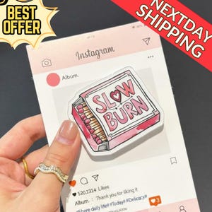 May include: A pink and white sticker with the words "SLOW BURN" in a box with a heart. The sticker is designed to look like a matchbox. The background is a mock Instagram post.