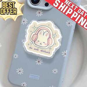 Könnte beinhalten: Hellblaue Handyhülle mit Gänseblümchenmuster und einem Pop-Socket mit einem Cartoon-Hasen mit Kopfhörern. Der Pop-Socket trägt den Text "do not disturb". Ein "Best Offer" Aufkleber ist sichtbar.