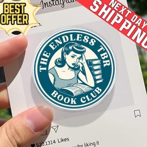 Puede incluir: Una pegatina redonda, verde azulado y blanca, con el texto "THE ENDLESS TBR BOOK CLUB" que rodea una ilustración vintage de una mujer leyendo. La pegatina está sujeta por una mano, con una pancarta de "BEST OFFER" y "NEXT DAY SHIPPING".