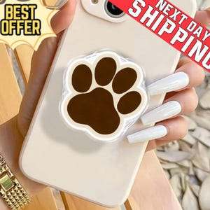 May include: A mobile phone with a brown paw print phone grip. The paw print has a white border. The phone is off-white. The image also includes the text "BEST OFFER" and "NEXT DAY SHIPPING".