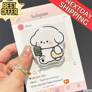 Puede incluir: Un charm de acrílico transparente con un perro de dibujos animados sosteniendo una taza de café y una bolsa. El charm está sobre un fondo rosa con temática de Instagram. También se ven las palabras "BEST OFFER" y "NEXTDAY SHIPPING".