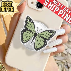 May include: A phone with a butterfly phone grip. The butterfly has green wings with black details. The phone is light-colored and has a clear phone grip. The image also includes the text "BEST OFFER" and "NEXT DAY SHIPPING".