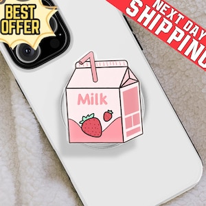May include: A pink strawberry milk carton phone grip with a straw, strawberry graphic, and the word "Milk". The phone grip is attached to a white phone. A "Best Offer" sticker is in the upper left corner.