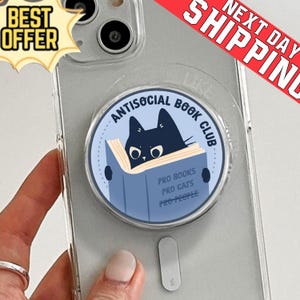 Könnte beinhalten: Ein klarer Telefonhalter mit einem kreisförmigen Design, das eine schwarze Katze zeigt, die ein blaues Buch liest. Der Text lautet "ANTISOCIAL BOOK CLUB" und "PRO BOOKS, PRO CATS, PRO PEOPLE". Ein "BEST OFFER" Aufkleber ist sichtbar.