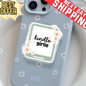 Può includere: Custodia per telefono azzurra con motivo a margherite e impugnatura pop-up. L'impugnatura mostra il testo "kindle girlie" in una cornice bianca con dettagli floreali. Include banner "Migliore offerta" e "Spedizione il giorno successivo".
