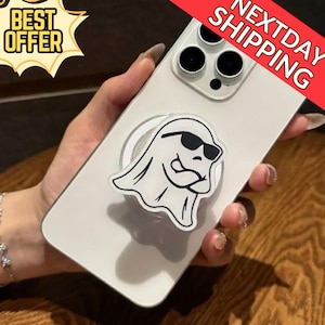 Puede incluir: Un teléfono inteligente blanco con un agarre para teléfono en forma de fantasma con gafas de sol negras y una cara sonriente. El teléfono tiene una cámara de triple lente. La imagen también incluye una pancarta de "BEST OFFER" y "NEXTDAY SHIPPING".