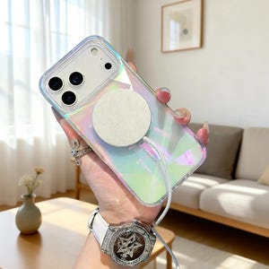 Könnte beinhalten: Schillernde Handyhülle mit einem weißen, kreisförmigen Ladepad. Die Hülle hat einen transparenten Rand und ist für ein Smartphone mit mehreren Kameralinsen konzipiert. Ein weißes Ladekabel ist mit dem Pad verbunden.