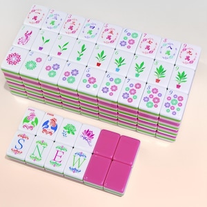 May include: A set of white Mahjong tiles with green, pink, and purple accents. The tiles feature various symbols, numbers, and Chinese characters. Some tiles have the letters S, N, E, and W. The set includes pink tiles.