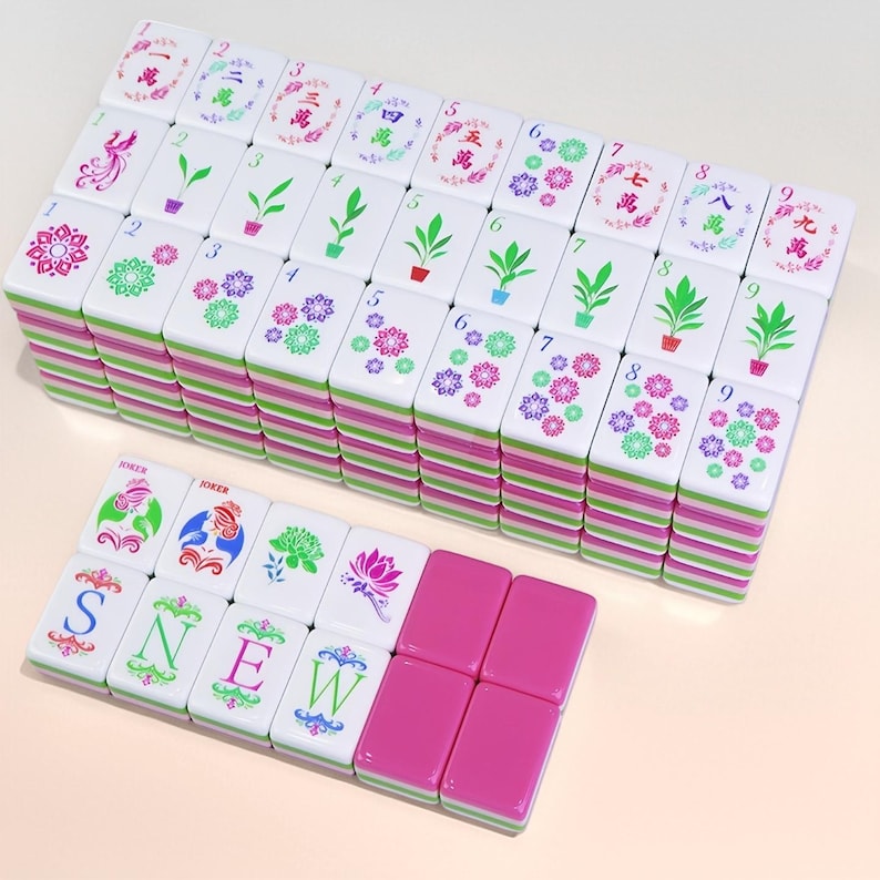 May include: A set of white Mahjong tiles with green, pink, and purple accents. The tiles feature various symbols, numbers, and Chinese characters. Some tiles have the letters S, N, E, and W. The set includes pink tiles.