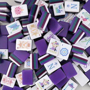 May include: A selection of purple and white Mahjong tiles. Some tiles feature colourful designs, including flowers, bamboo, and a woman with the word "Joker". Other tiles have the letter "N" or stripes. The tiles are scattered, creating a visually appealing arrangement.