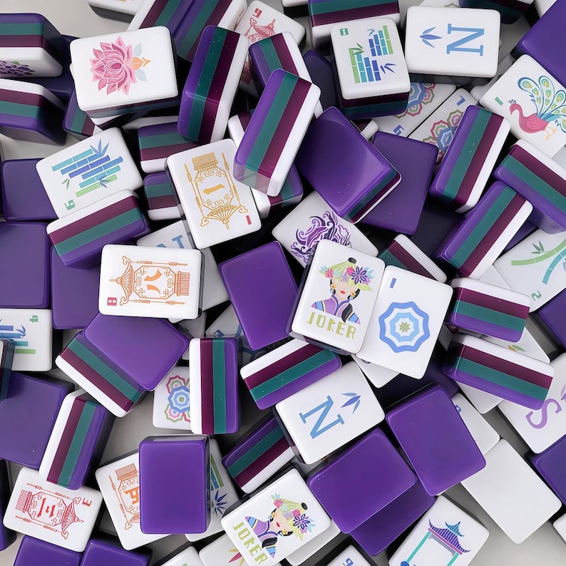 May include: A selection of purple and white Mahjong tiles. Some tiles feature colourful designs, including flowers, bamboo, and a woman with the word "Joker". Other tiles have the letter "N" or stripes. The tiles are scattered, creating a visually appealing arrangement.