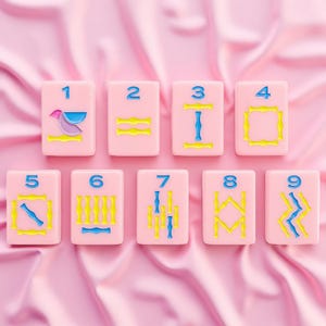 May include: A set of nine rectangular pink tiles arranged in two rows, each featuring a blue numeral from one to nine at the top and various yellow and blue geometric or abstract symbols below, all presented with a smooth, matte finish.