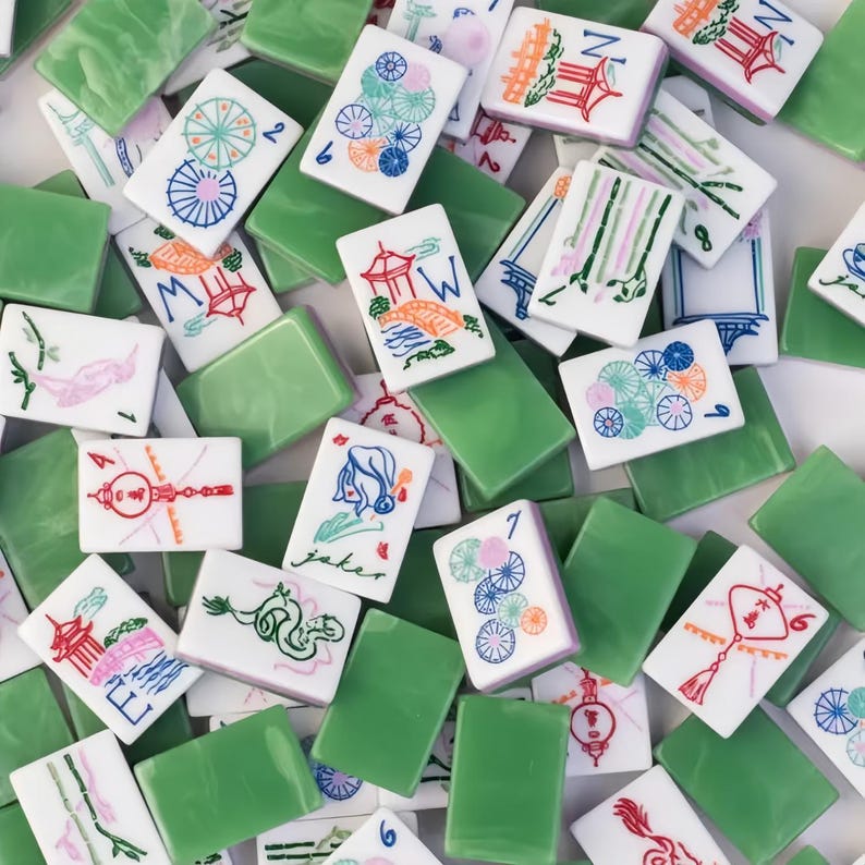 May include: A collection of white and green Mahjong tiles. The white tiles feature colorful illustrations of pagodas, flowers, and other symbols. The green tiles are solid and rectangular. The tiles are scattered, creating a visually appealing pattern.