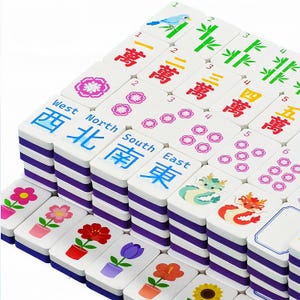 May include: A collection of white Mahjong tiles with purple striped edges. The tiles feature various symbols, numbers, and Chinese characters in red and blue. Some tiles display flowers, dragons, and birds. The game set is arranged in stacks.