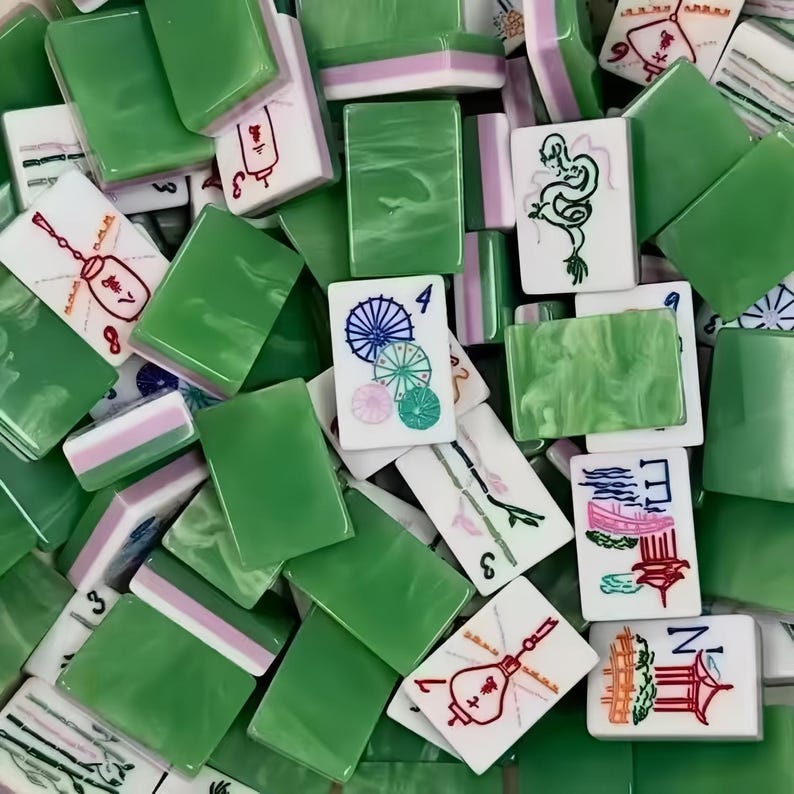 May include: A collection of green and white Mahjong tiles. The tiles feature various symbols, numbers, and illustrations in red, black, and green. Some tiles are solid green, while others have pink and white accents. The game pieces are scattered.