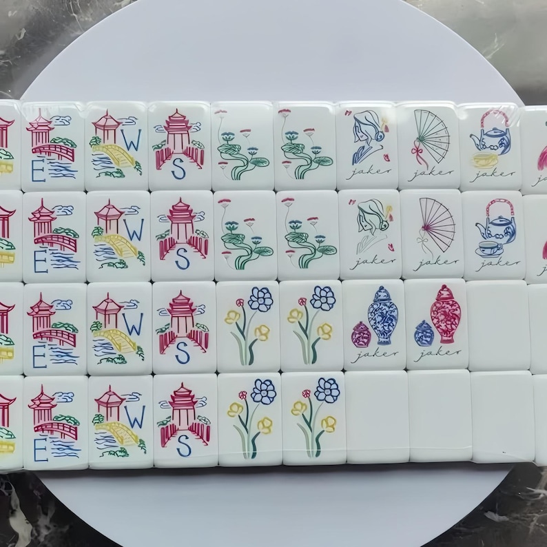 May include: A collection of white Mahjong tiles with colorful illustrations. The tiles feature images of pagodas, bridges, flowers, and teapots. Some tiles have the letter "S" or the word "joker" on them.