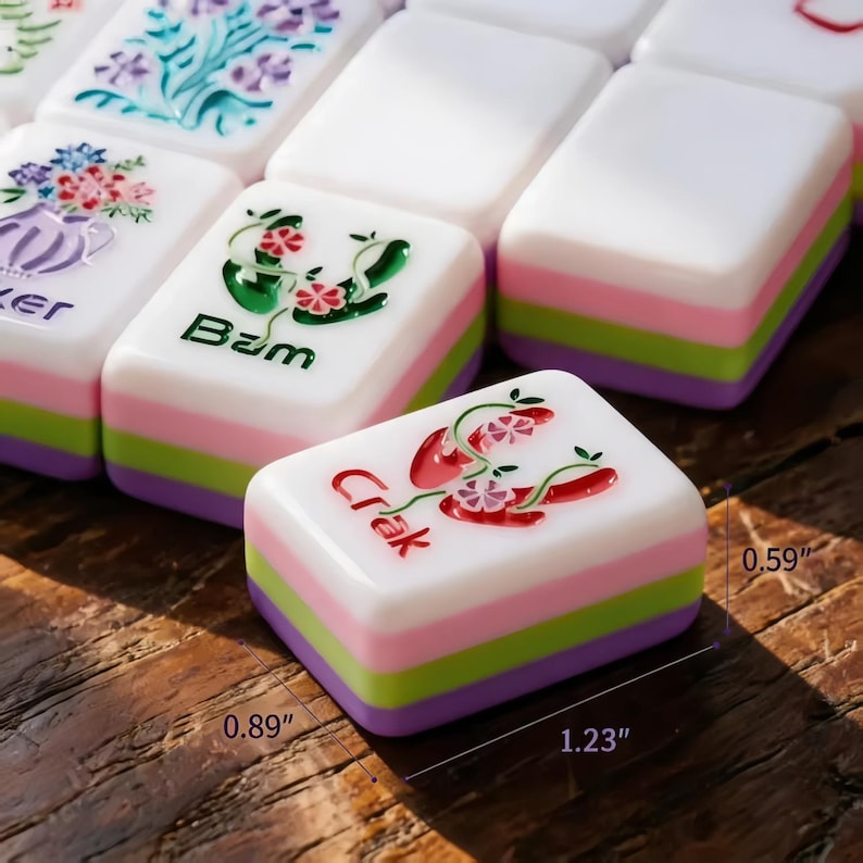 May include: Close-up of colourful Mahjong tiles. The tiles are white with a layered design of pink, green, and purple. The tiles have various illustrations and text, including "Crak" and "Bam". The tiles measure 3.1 cm x 2.3 cm x 1.5 cm.