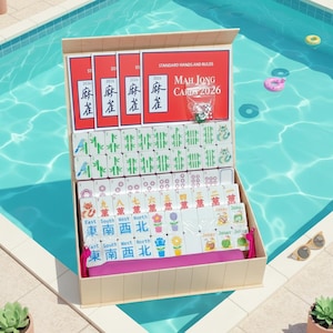 May include: Open mahjong set with tiles and dice, displayed in a box. The box is beige with a pink interior. The tiles are white with various symbols and characters. The set is labeled "MAH JONG CARDS 2026".