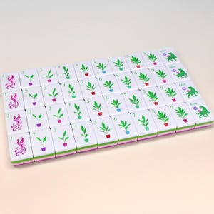 May include: A set of white Mahjong tiles with green, purple, and red plant illustrations and numbers. The tiles are arranged in a rectangular pattern. Some tiles have the word "BAM" and a green illustration of a dragon.