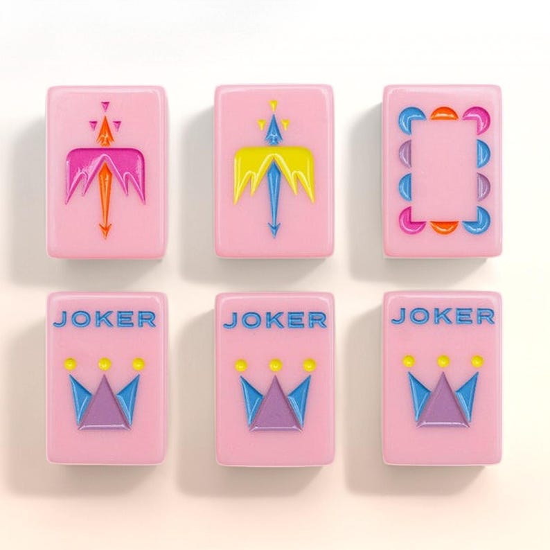 May include: Six rectangular pink tiles with rounded corners. The top row features two tiles with stylized orange and yellow arrow designs and one tile with a colorful crescent border. The bottom row shows three tiles labeled JOKER with a crown icon.