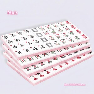 May include: A set of white mahjong tiles with pink backs, featuring various black, red, and green engraved symbols, characters, and floral designs. The tiles are arranged in stacked rows. Text on the image includes Pink and Size: 30*22.5*12.5mm.