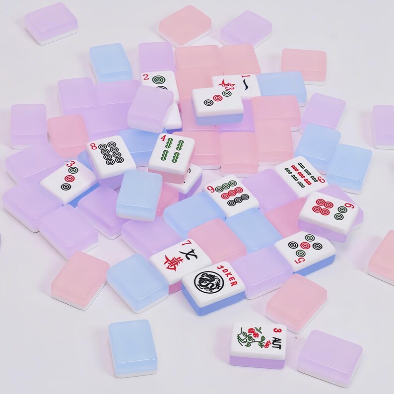 May include: A collection of rectangular mahjong tiles in translucent pastel shades of pink, blue, and purple. Some tiles feature printed numbers, symbols, and characters in black, red, and green ink, including a Joker tile and a floral design.