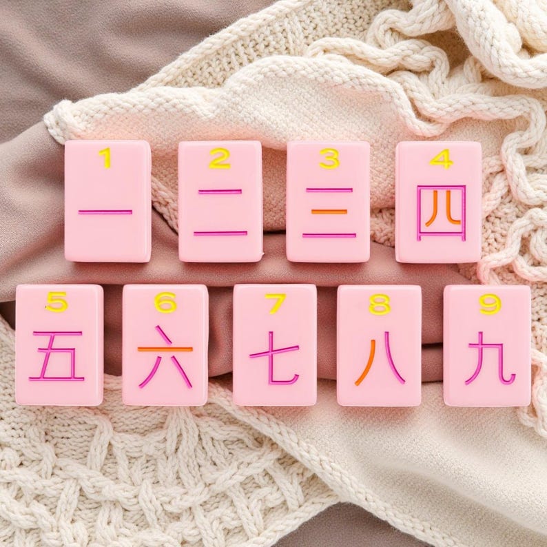May include: A set of nine rectangular light pink tiles arranged in two rows. Each tile features a yellow Arabic numeral from 1 to 9 at the top and a corresponding Chinese character in orange or pink below, representing the numbers one through nine.
