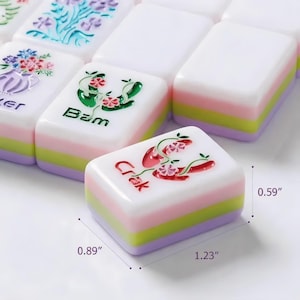 May include: A set of colourful Mahjong tiles. Each tile is white with a colourful design and text. The tiles are 2.26 cm wide, 3.12 cm long, and 1.5 cm thick. The tiles have a pink, green, and purple base.