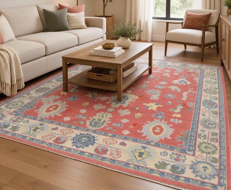 May include: A rectangular area rug featuring a vibrant coral red field with a central medallion pattern in shades of light blue, cream, and sage green. The rug has a wide cream-colored border with blue and green floral motifs and geometric shapes.