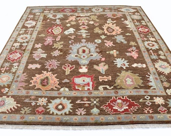 May include: A large, rectangular brown rug with a detailed floral design in red, blue, pink, and beige. The rug features a border with a repeating geometric pattern and a fringe. Ideal for a living room or bedroom, it measures approximately 300cm x 200cm.