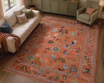 May include: A large rectangular area rug featuring a vibrant terracotta orange background with a multi-coloured floral pattern in shades of blue, green, and cream. The rug has a wide border with a repeating geometric and floral design motif.