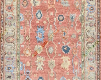 May include: A rectangular rug with a central field of coral red, adorned with intricate floral and geometric patterns in shades of blue, beige, and green. The rug has a detailed border with similar motifs, creating a cohesive design. The rug's dimensions are not visible.