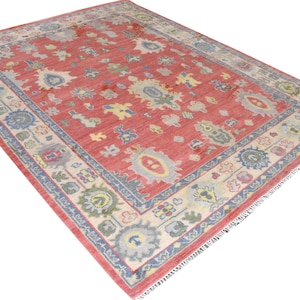 Vintage Oushak rug in pink-red wool with pale blue border and ivory floral motifs; hand-knotted, handmade wool rug.