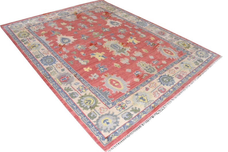 Vintage Oushak rug in pink-red wool with pale blue border and ivory floral motifs; hand-knotted, handmade wool rug.