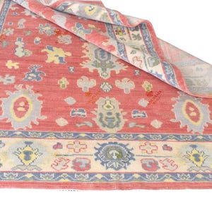 Vintage Oushak rug in pink-red wool with pale blue border and ivory floral motifs; hand-knotted, handmade wool rug.