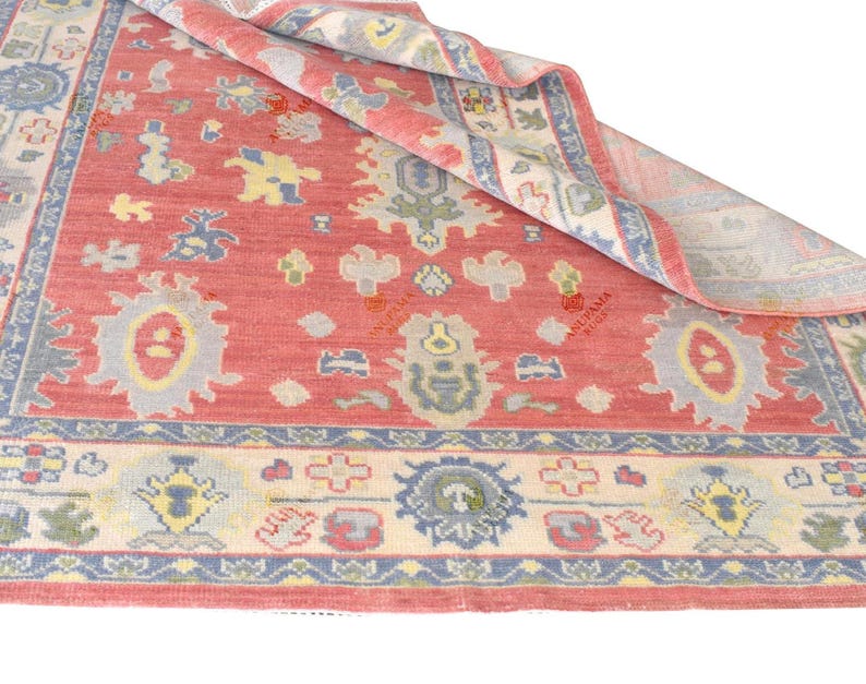 Vintage Oushak rug in pink-red wool with pale blue border and ivory floral motifs; hand-knotted, handmade wool rug.