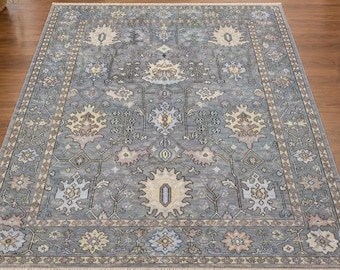 May include: A rectangular area rug featuring a slate blue background with intricate floral and geometric patterns in cream, light blue, and soft pink. The rug has a wide decorative border and short white fringe along the top and bottom edges.