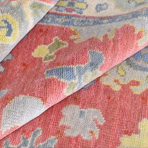 Vintage Oushak rug in pink-red wool with pale blue border and ivory floral motifs; hand-knotted, handmade wool rug.