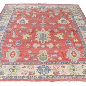 Vintage Oushak rug in pink-red wool with pale blue border and ivory floral motifs; hand-knotted, handmade wool rug.