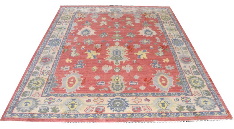 Vintage Oushak rug in pink-red wool with pale blue border and ivory floral motifs; hand-knotted, handmade wool rug.