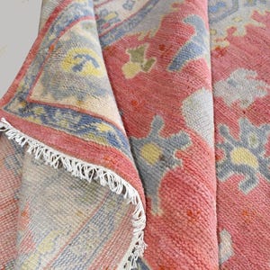 Vintage Oushak rug in pink-red wool with pale blue border and ivory floral motifs; hand-knotted, handmade wool rug.