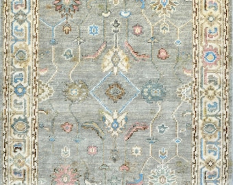 May include: A rectangular area rug featuring a grey field with a central floral medallion and intricate botanical motifs in shades of blue, pink, cream, and brown. The rug is framed by a wide, detailed border with geometric patterns.
