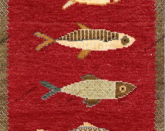 May include: A rectangular red rug featuring eight distinct fish motifs arranged in a vertical column. Each fish displays a unique pattern, colour, and texture, including shades of beige, brown, and green. The rug has a brown border and fringe.