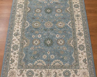 May include: A rectangular area rug featuring a dusty blue central field adorned with intricate floral medallions and scrolling vine patterns in cream, sage green, and tan, framed by a wide cream border with detailed botanical motifs.
