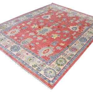 Vintage Oushak rug in pink-red wool with pale blue border and ivory floral motifs; hand-knotted, handmade wool rug.