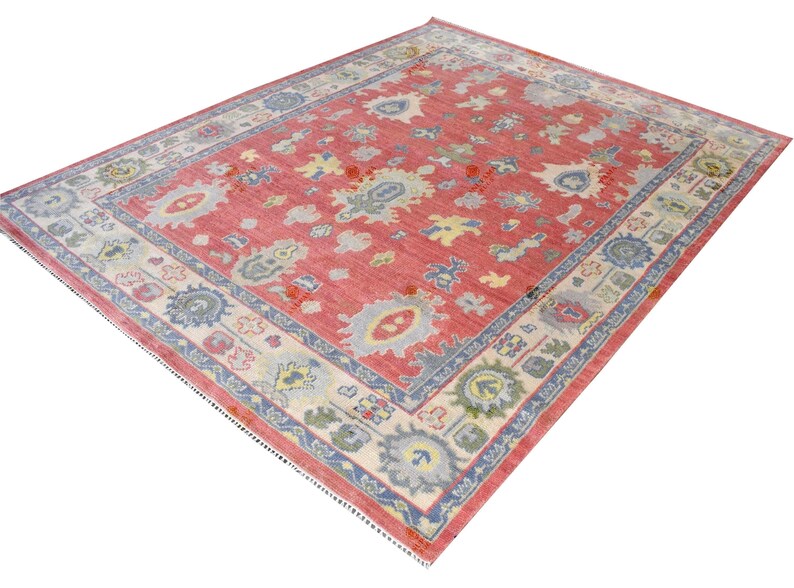 Vintage Oushak rug in pink-red wool with pale blue border and ivory floral motifs; hand-knotted, handmade wool rug.